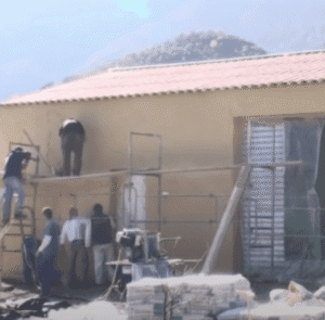 Équipe d’artisans appliquant l’enduit de façade sur un bâtiment, échafaudage en place et projection mécanique du crépi — rénovation des murs extérieurs.