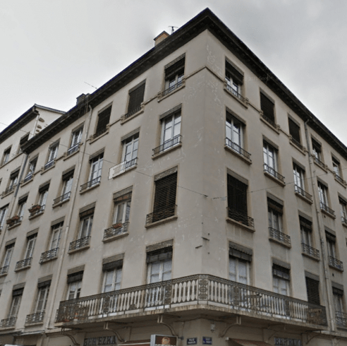 Immeuble d’angle ancien avec façade ternie, enduits fissurés et garde-corps oxydés, avant ravalement et restauration de bâtiment.