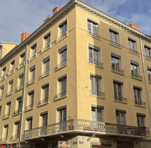 Façade d’immeuble d’angle entièrement rénovée, enduits ocre neufs, encadrements et garde-corps restaurés après ravalement — restauration de bâtiment à Lyon.