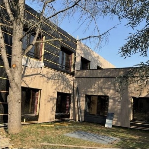 Façade en rénovation avec isolation par l’extérieur, pare-pluie noir et pose d’un bardage bois vertical — chantier de restauration de bâtiment.