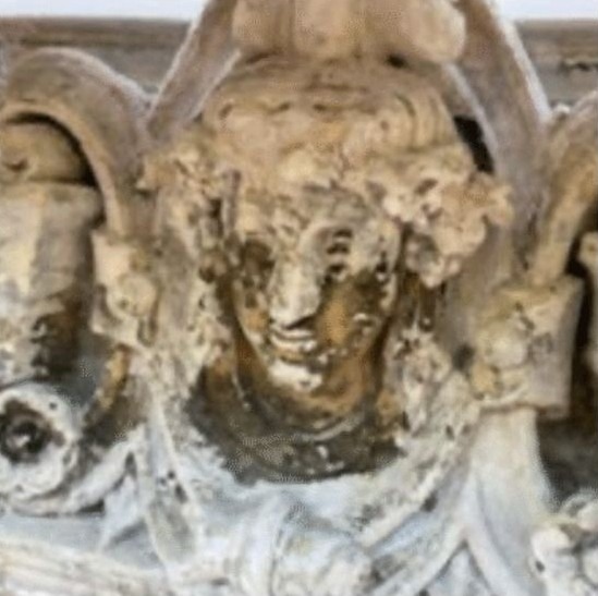 Mascaron en pierre très encrassé et écaillé sur façade ancienne, détail sculpté à restaurer lors d’une restauration de bâtiment.