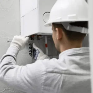 Technicien en maintenance intervenant sur une chaudière murale au gaz : réglage des vannes et contrôle de l’installation de chauffage.