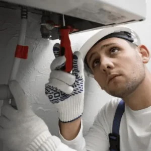 Plombier professionnel réparant un chauffe-eau/chaudière murale : inspection des tuyaux et entretien du système de chauffage domestique.