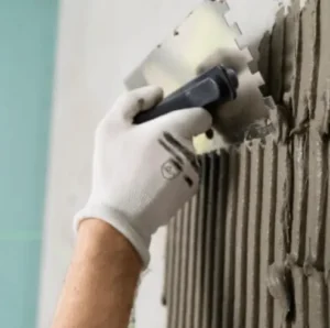 Application de colle à carrelage à la spatule crantée sur un mur avant pose des carreaux